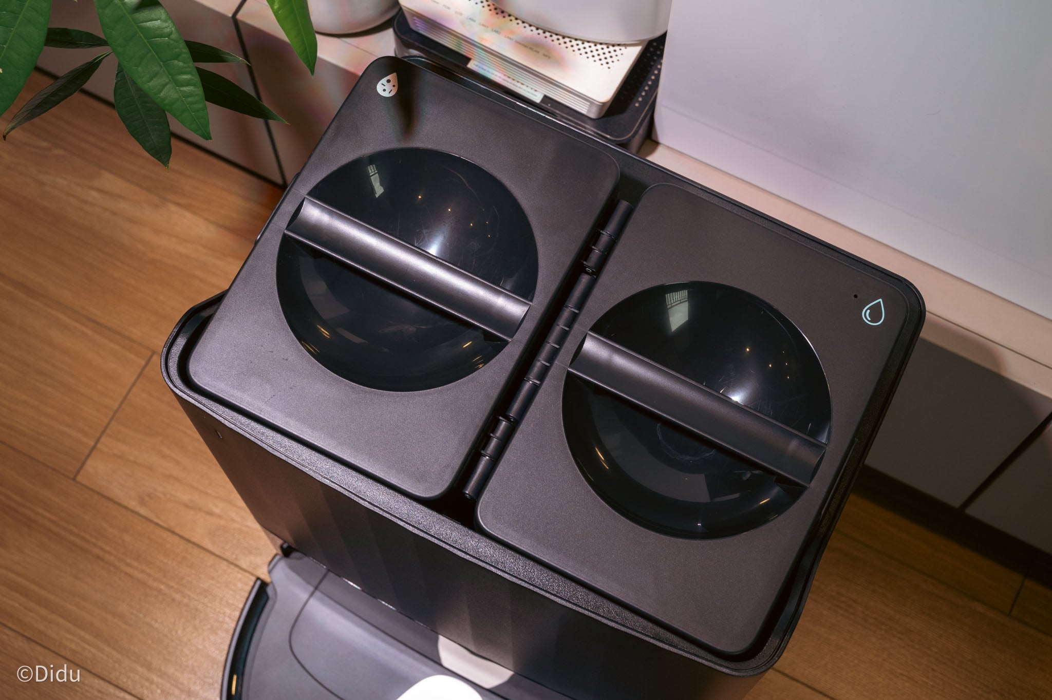 Túi chứa rác được đặt bên trong nắp màu đen, trong khi hai bình chứa nước ở bên trên đỉnh